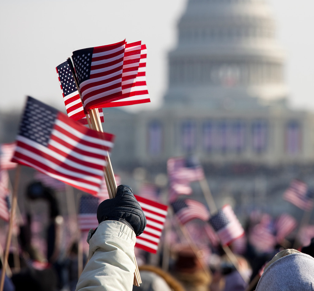 American flags wave in the foreground with the U.S. Capitol in the background during a presidential inauguration.