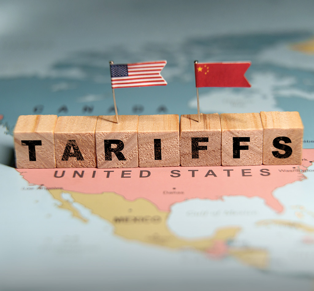Wooden blocks spelling TARIFFS placed on a map of the United States with US and China flags.